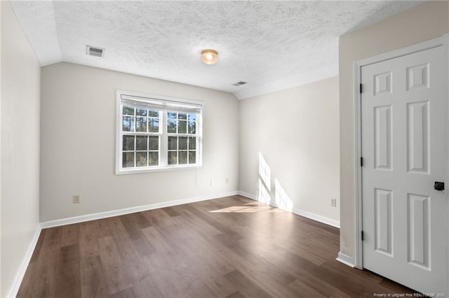 empty room with a textured ceiling, dark hardwood / wood-style flooring, and lofted ceiling