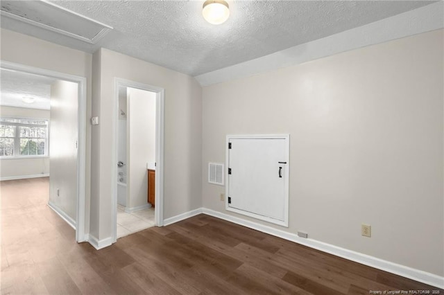 empty room featuring a textured ceiling, hardwood / wood-style flooring, and vaulted ceiling