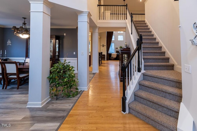 stairs with ornate columns, a chandelier, wood-type flooring, and ornamental molding