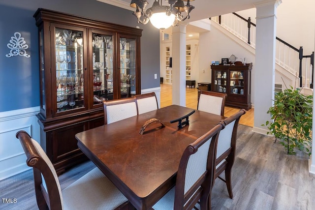 dining area with decorative columns, crown molding, an inviting chandelier, and hardwood / wood-style flooring