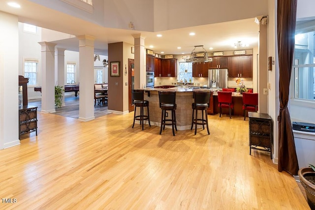 kitchen featuring a kitchen bar, appliances with stainless steel finishes, ornate columns, a high ceiling, and light hardwood / wood-style floors