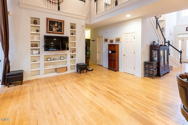 living room featuring built in features, a towering ceiling, and light wood-type flooring