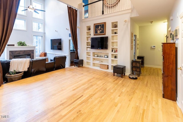 living room with a towering ceiling, light hardwood / wood-style floors, built in features, and ceiling fan