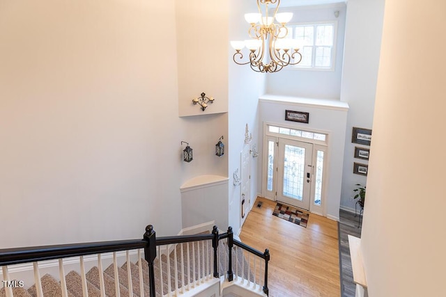 foyer with a towering ceiling, wood-type flooring, a wealth of natural light, and an inviting chandelier