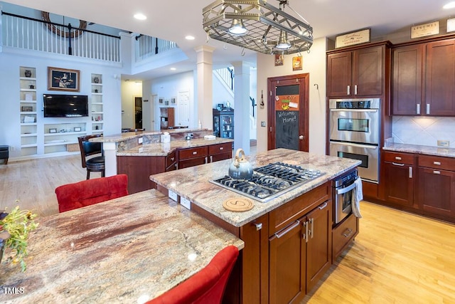 kitchen featuring decorative columns, a breakfast bar, stainless steel appliances, decorative light fixtures, and a center island