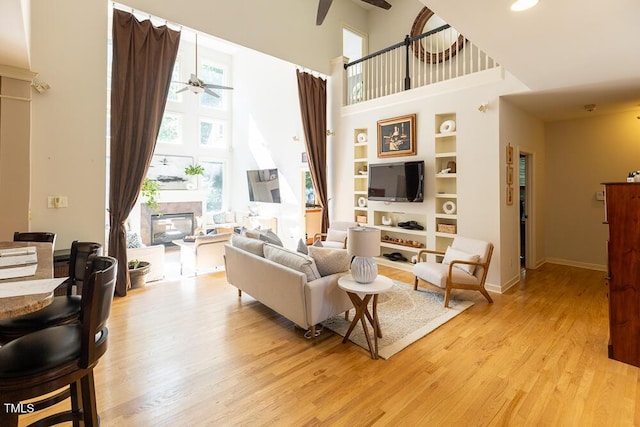 5240 Indigo Moon Way, Raleigh, NC 27613 - living area featuring a ceiling fan, a glass covered fireplace, a high ceiling, light wood finished floors, and built in features