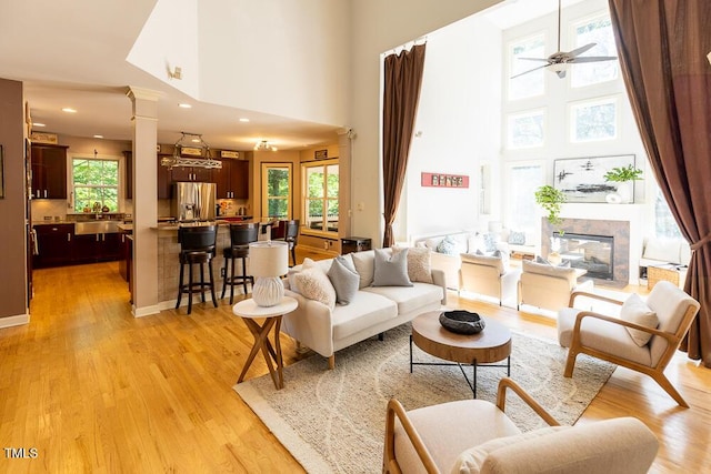 5240 Indigo Moon Way, Raleigh, NC 27613 - living area with a towering ceiling, light wood-style floors, decorative columns, a ceiling fan, and a tiled fireplace