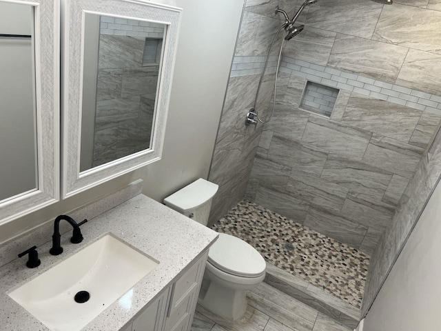 bathroom with a tile shower, vanity, and toilet