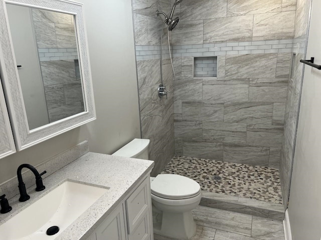 bathroom with a tile shower, vanity, and toilet