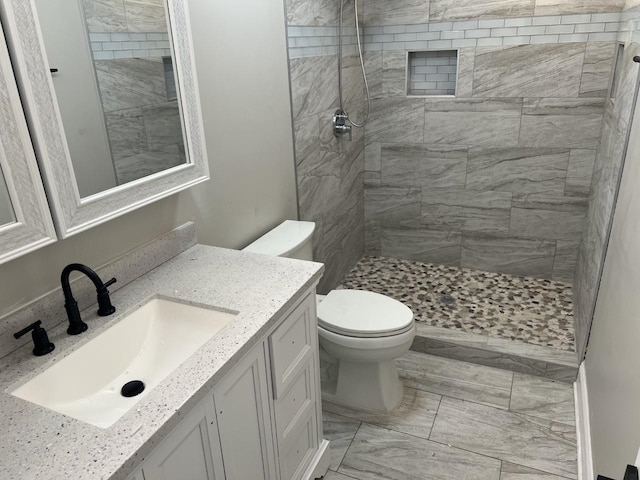 bathroom featuring a tile shower, vanity, and toilet