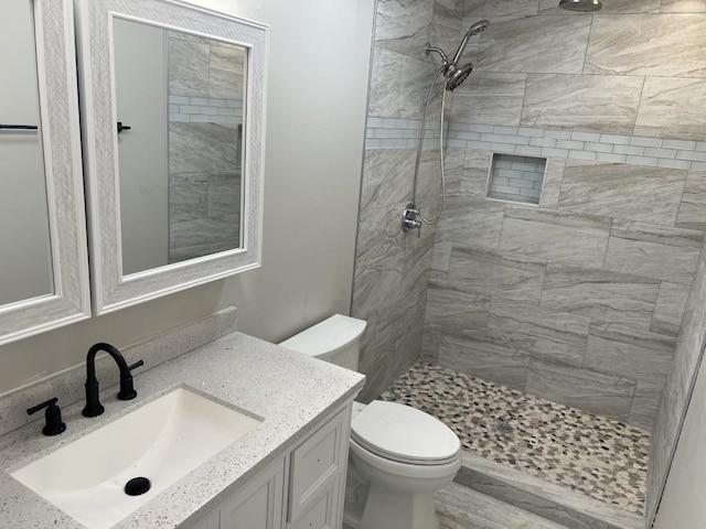 bathroom with a tile shower, vanity, and toilet