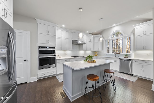 kitchen featuring appliances with stainless steel finishes, hanging light fixtures, dark hardwood / wood-style floors, a kitchen island, and white cabinetry