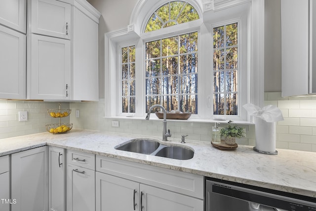 kitchen with white cabinets, light stone counters, sink, stainless steel dishwasher, and backsplash