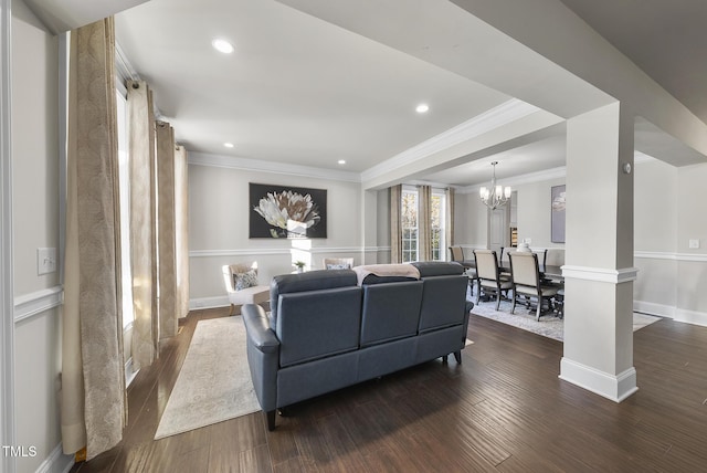 living room featuring dark wood-type flooring, crown molding, a chandelier, and ornate columns