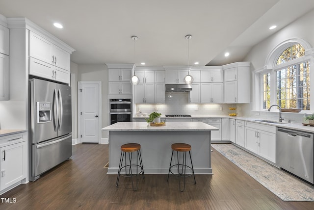 kitchen featuring stainless steel appliances, sink, a center island, white cabinetry, and hanging light fixtures