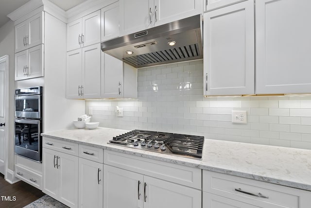 kitchen with appliances with stainless steel finishes, light stone counters, dark hardwood / wood-style floors, white cabinets, and tasteful backsplash