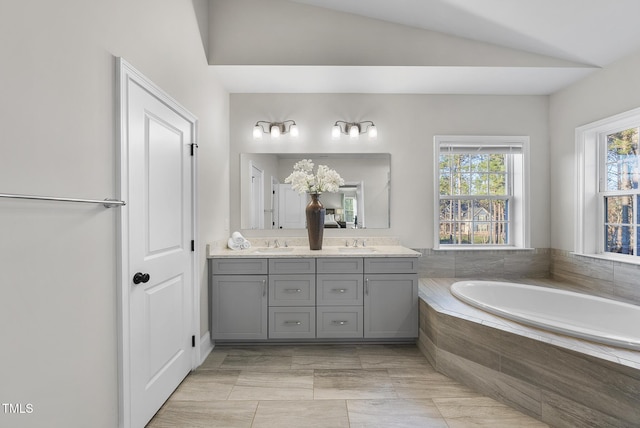 bathroom with vaulted ceiling, tiled bath, and vanity