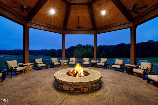 patio terrace at dusk with a gazebo, an outdoor living space with a fire pit, ceiling fan, and a water view