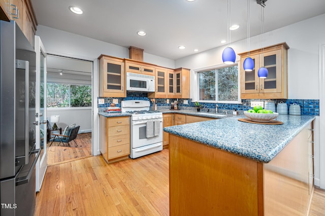 kitchen with white appliances, light hardwood / wood-style flooring, hanging light fixtures, stone countertops, and kitchen peninsula