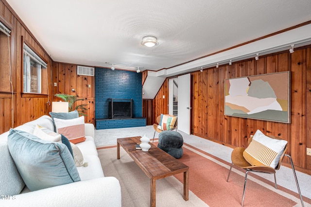 carpeted living room with rail lighting, a brick fireplace, and wood walls