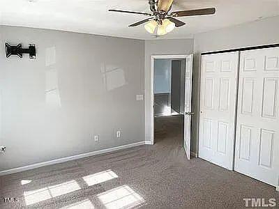 unfurnished bedroom with ceiling fan, a closet, and dark colored carpet