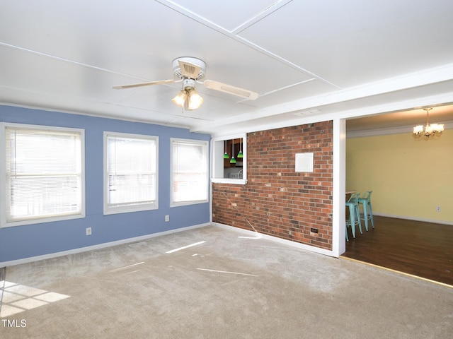 unfurnished room with a wealth of natural light, carpet floors, brick wall, and ceiling fan with notable chandelier