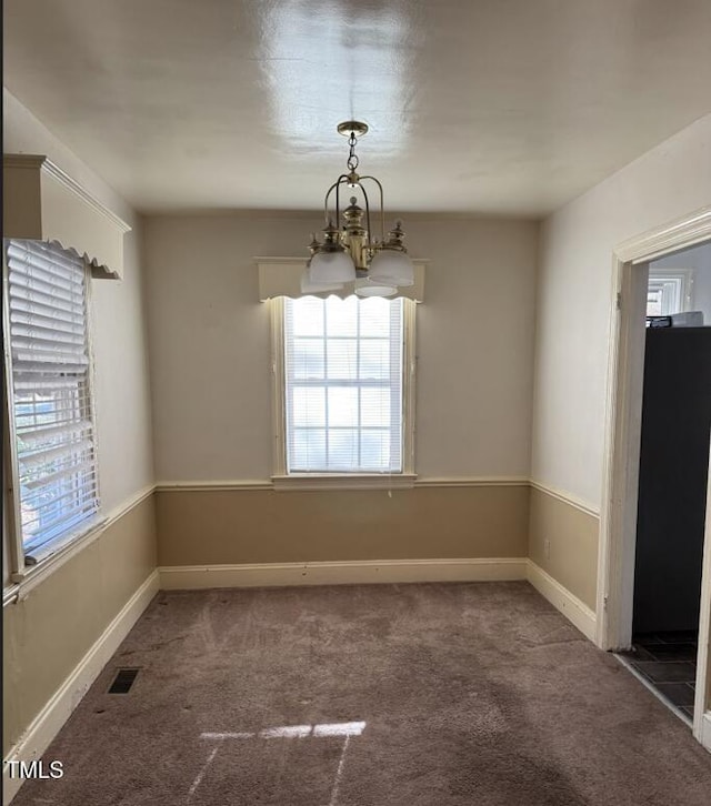 spare room featuring plenty of natural light, an inviting chandelier, and dark carpet