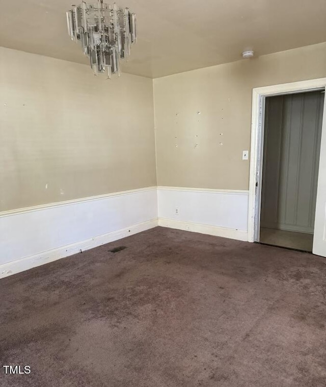 carpeted empty room with an inviting chandelier