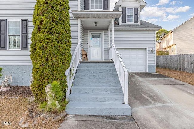 view of exterior entry with a garage, concrete driveway, and fence