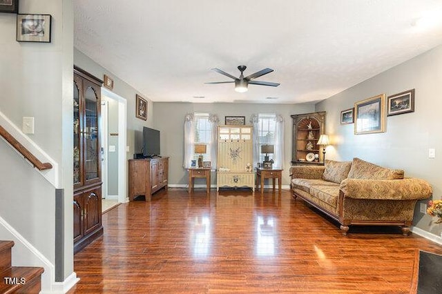 living room featuring a ceiling fan, wood finished floors, baseboards, and stairs