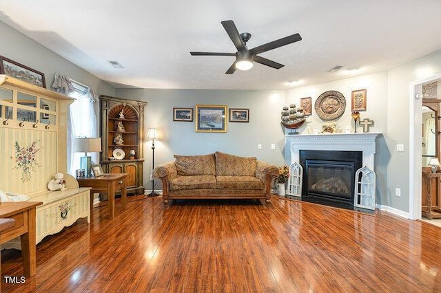 living room featuring a glass covered fireplace, wood finished floors, a ceiling fan, and baseboards