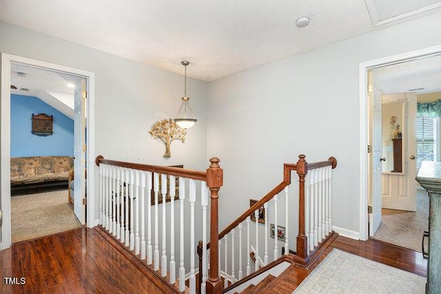 corridor with baseboards, an upstairs landing, and wood finished floors