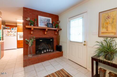 living room featuring crown molding, a brick fireplace, and light tile patterned floors