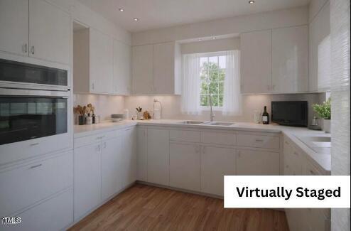 kitchen featuring sink, stainless steel oven, light wood-type flooring, decorative backsplash, and white cabinets