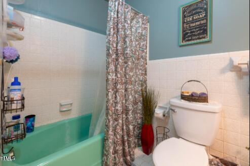 bathroom with shower / tub combo with curtain, toilet, and tile walls