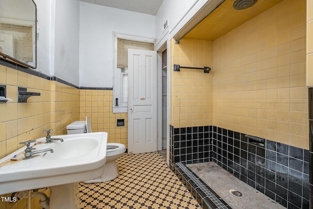 bathroom featuring a tile shower, toilet, tile walls, and sink