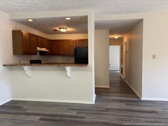 kitchen featuring black refrigerator, a kitchen breakfast bar, kitchen peninsula, and dark hardwood / wood-style floors