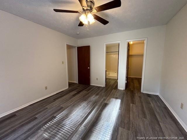 unfurnished bedroom featuring ensuite bath, ceiling fan, a spacious closet, dark hardwood / wood-style floors, and a closet