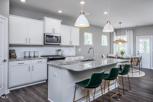 kitchen with stainless steel appliances, sink, a center island with sink, white cabinets, and hanging light fixtures