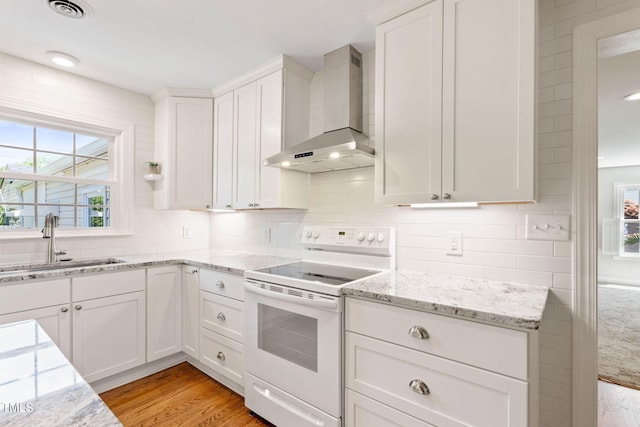 kitchen with sink, wall chimney range hood, light hardwood / wood-style flooring, electric stove, and white cabinets