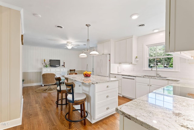 kitchen featuring sink, a kitchen island, decorative light fixtures, white appliances, and white cabinets