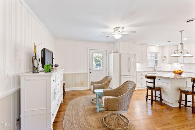 living area with ceiling fan, a healthy amount of sunlight, light wood-type flooring, and ornamental molding