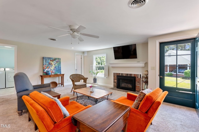 living room with washer and clothes dryer, ceiling fan, light colored carpet, and a brick fireplace