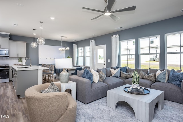 living room with sink, ceiling fan with notable chandelier, and light hardwood / wood-style flooring