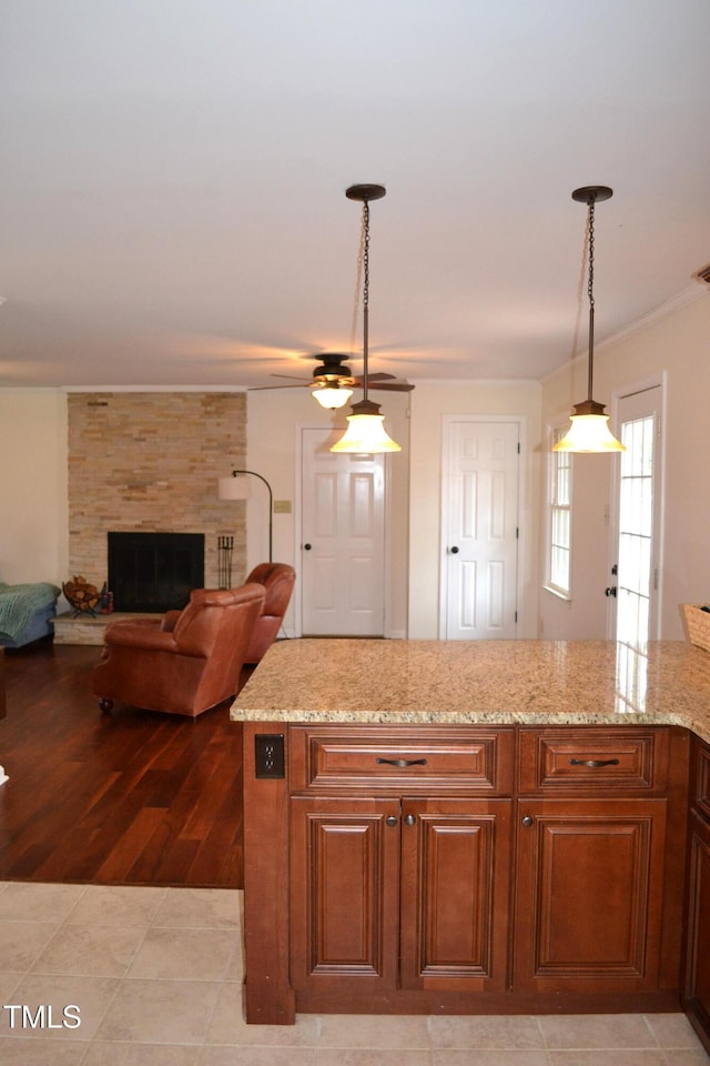 kitchen featuring a stone fireplace, hanging light fixtures, ceiling fan, light tile patterned flooring, and light stone counters