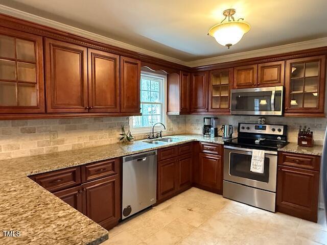 kitchen with decorative backsplash, light stone counters, ornamental molding, stainless steel appliances, and sink