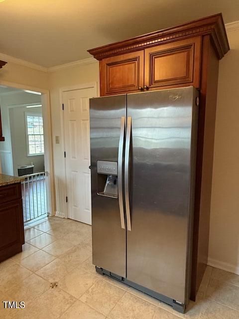 kitchen featuring stainless steel fridge, light tile patterned flooring, light stone countertops, and crown molding