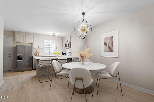 dining room with light wood-type flooring, a notable chandelier, and sink