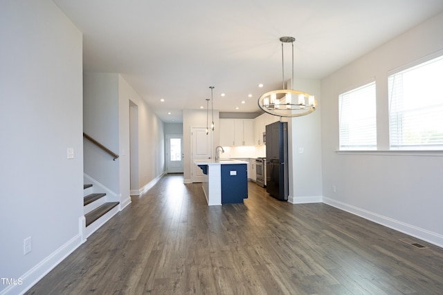 kitchen featuring hanging light fixtures, an inviting chandelier, black refrigerator, white cabinets, and a center island with sink