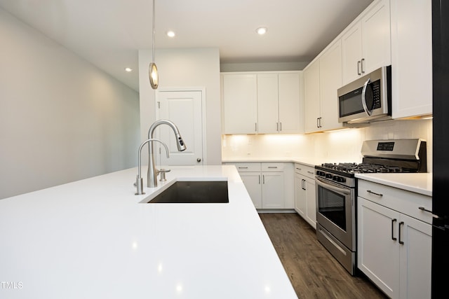 kitchen with dark hardwood / wood-style flooring, stainless steel appliances, sink, pendant lighting, and white cabinets